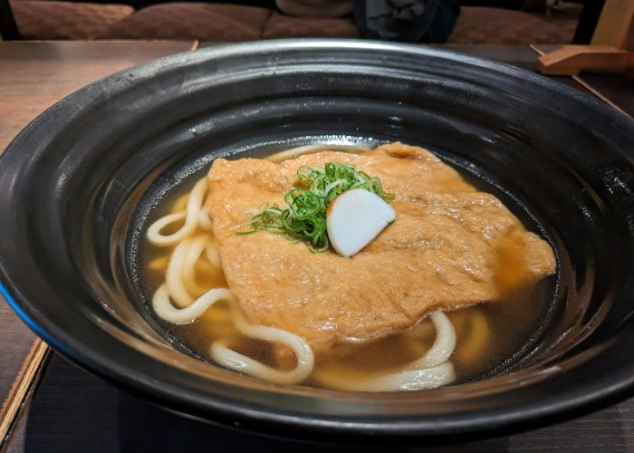 A serving of kitsune udon at Tsuru Ton Tan, with fried tofu, fishcake, and udon noodles in a broth.